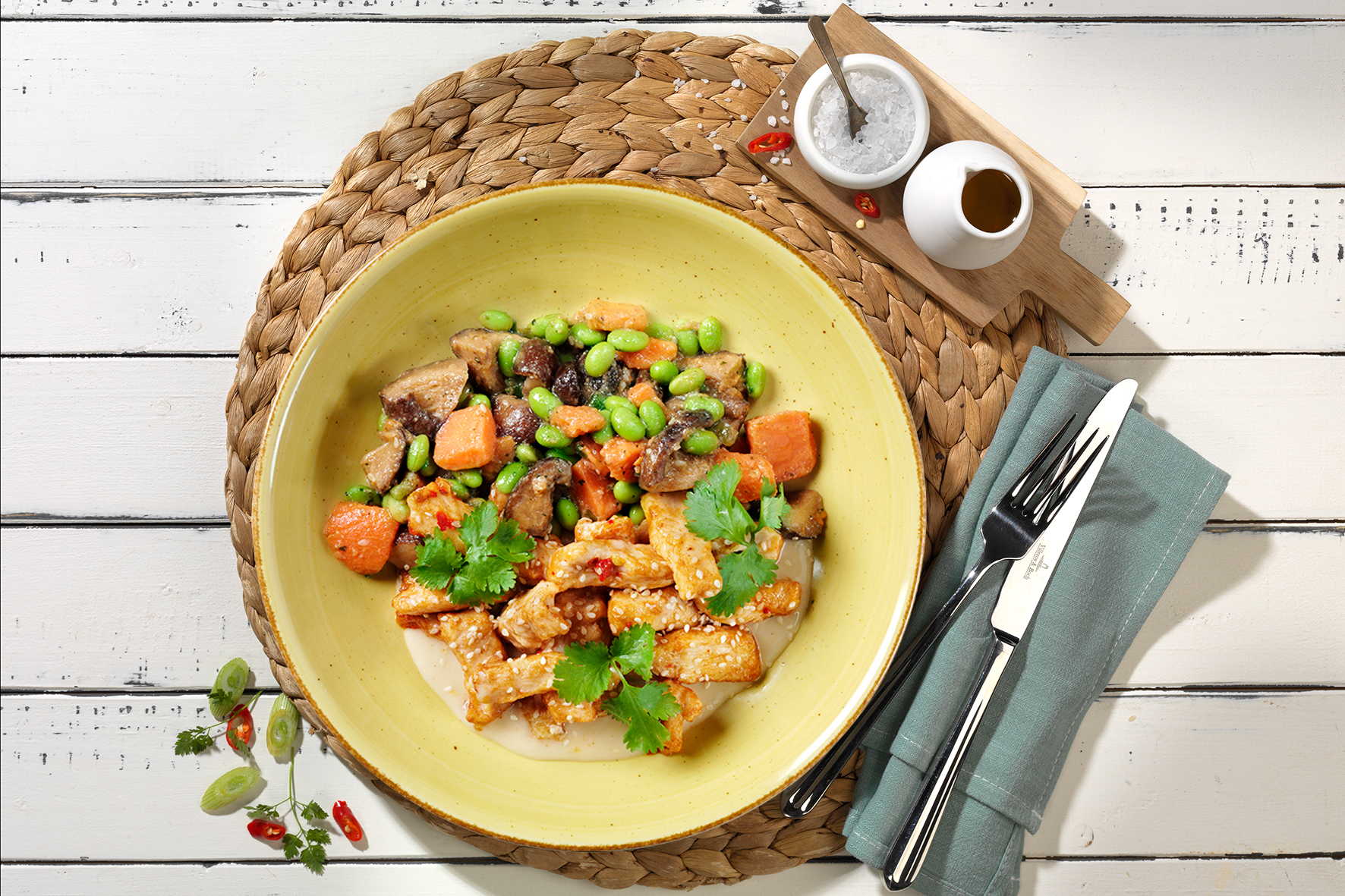 Spicy Chicken Bowl von Hofmanns Shop, mit Tofu, Gemüse und Koriander auf einer Matte, erinnert an die lebendige asiatische Küche.